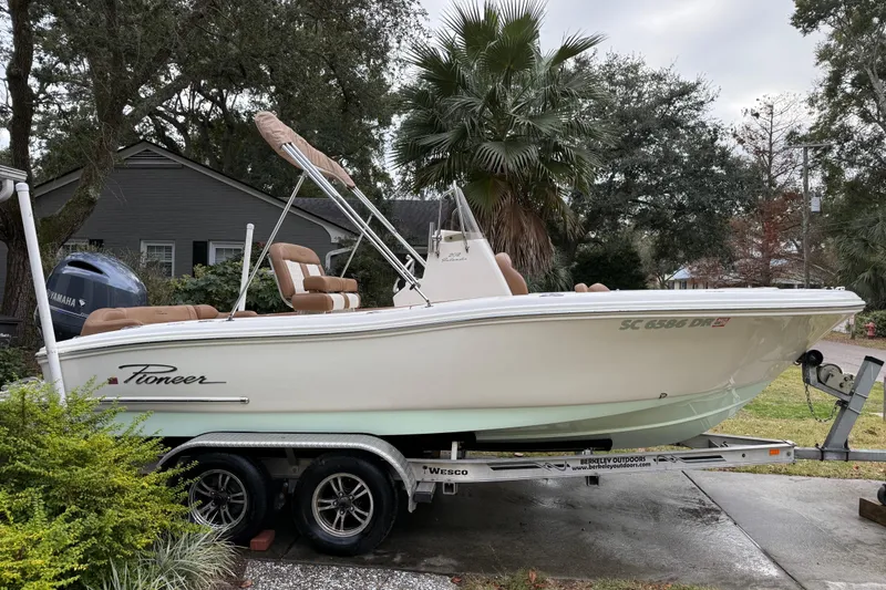 Slide: The Image of 2021 Pioneer 202 Islander boat on trailer, parked outdoors near trees and a house. - 2