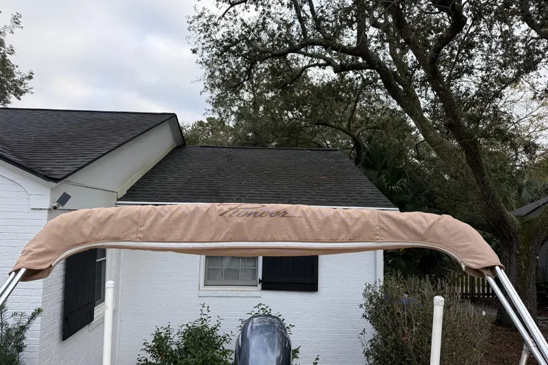 Slide: The Image of 2021 Pioneer 202 Islander boat with canopy, in front of a white house and trees. - 28