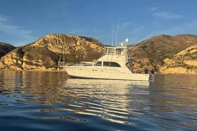Slide: The Image of 1979 Bertram 46.6 Sport Fisher yacht on calm water with scenic rocky backdrop. - 2