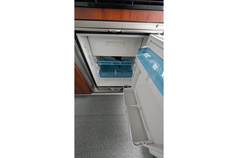 Slide: The Image of Open refrigerator inside 2022 Hewscraft Pacific Explorer boat, featuring blue storage compartments. - 32