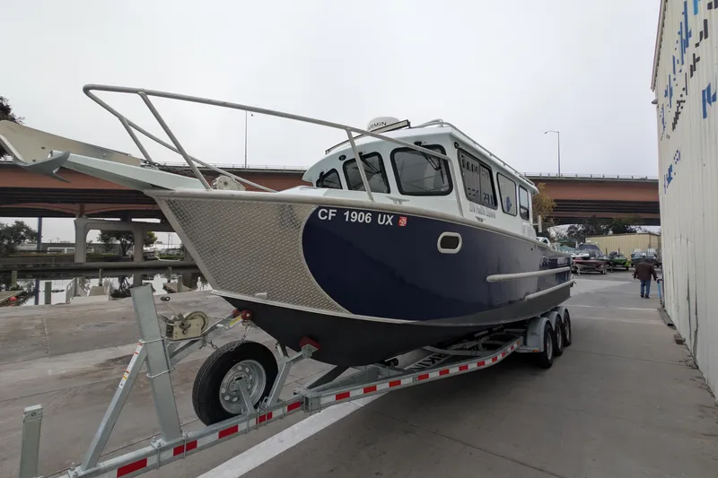 Slide: The Image of 2022 Hewscraft Pacific Explorer boat on trailer near bridge and building. - 8