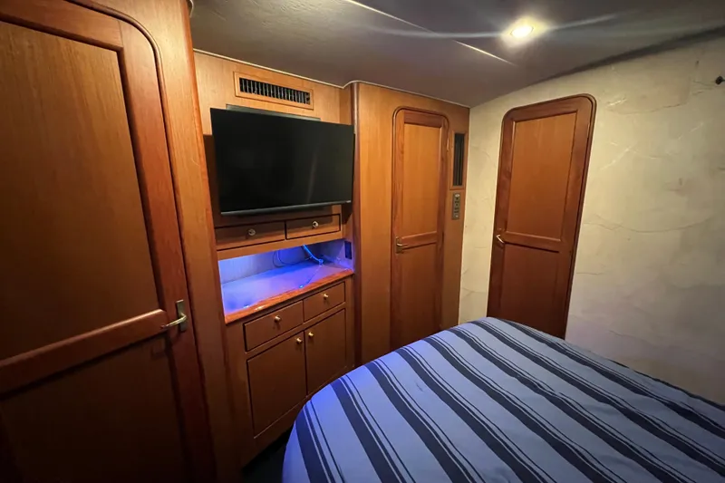 Slide: The Image of 1999 Ocean Yachts 56 Super Sport cabin with TV, wooden cabinetry, and striped bedding. - 46