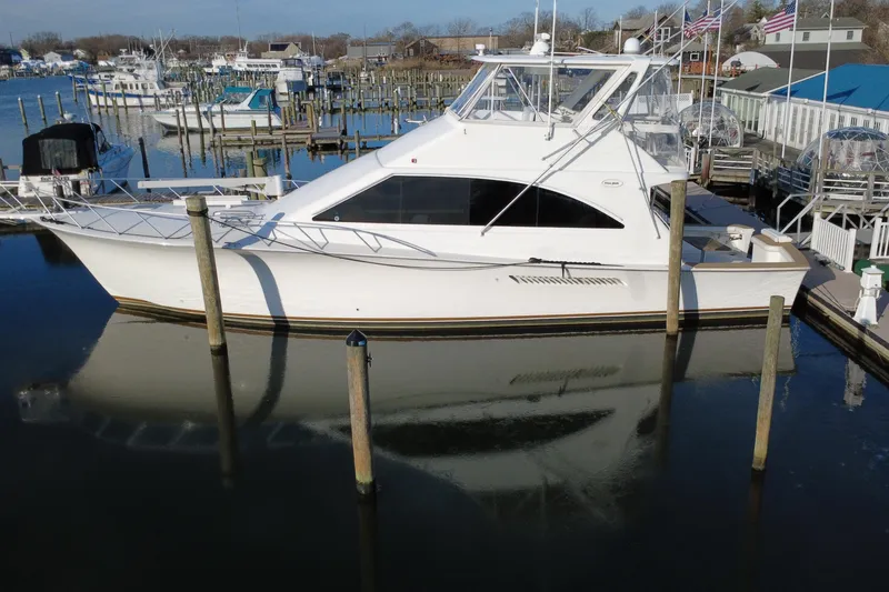 Slide: The Image of 1999 Ocean Yachts 56 Super Sport docked at a marina, reflecting on calm water. - 5