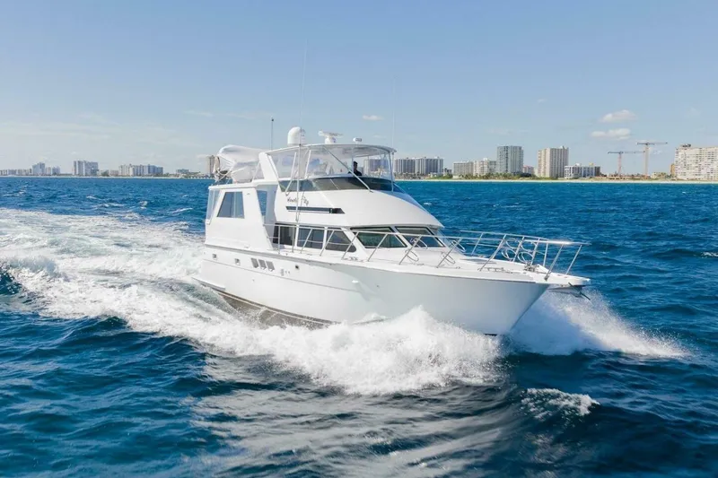 The Image of 1999 Hatteras 52 Sport Deck Motor Yacht cruising on blue ocean near city skyline. - 0