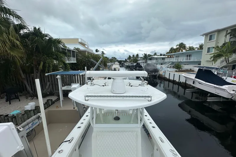 Slide: The Image of 2012 Yellowfin 32 Offshore boat docked in a residential canal, surrounded by palm trees and houses. - 13
