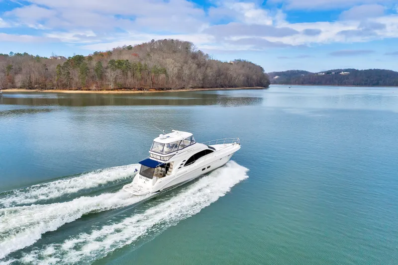 Slide: The Image of 2006 Sea Ray 58 Sedan Bridge yacht cruising on a serene lake with wooded shoreline. - 4