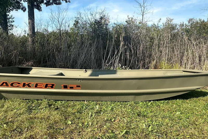 The Image of 2026 Tracker Grizzly 12 Jon boat on grass, surrounded by tall reeds and trees. - 0