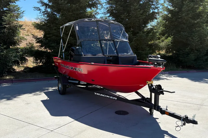 Slide: The Image of 2026 Tracker Pro Guide V-16 WT boat on trailer, parked outdoors, surrounded by trees. - 2