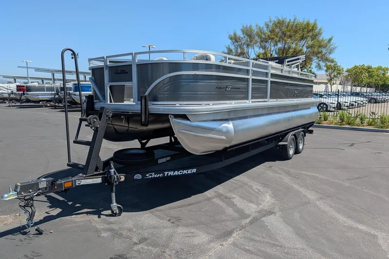 Slide: The Image of 2026 Sun Tracker Fishin' Barge 22 DLX pontoon boat on trailer in parking lot. - 1