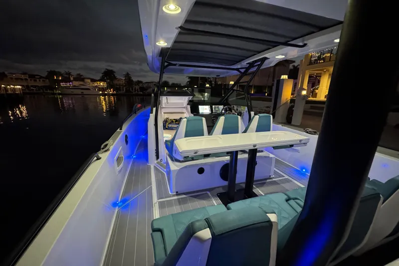 Slide: The Image of 2021 Axopar 37 boat interior with blue LED lighting at night, docked by waterfront homes. - 28