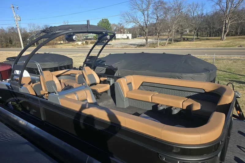 Slide: The Image of 2026 Qwest 8524 Q3XA pontoon boat with tan seating and black frame, parked outdoors. - 18