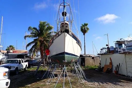 Slide: The Image of 1987 Irwin 38 sailboat on stands, surrounded by palm trees and vehicles. - 1