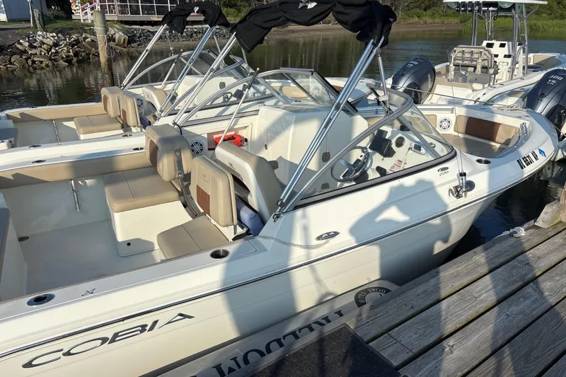 Slide: The Image of 2024 Cobia 220 Dual Console boat docked, featuring spacious seating and modern design. - 2