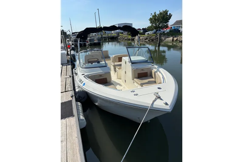 Slide: The Image of 2024 Cobia 220 Dual Console boat docked in a marina, featuring sleek design and spacious seating. - 3