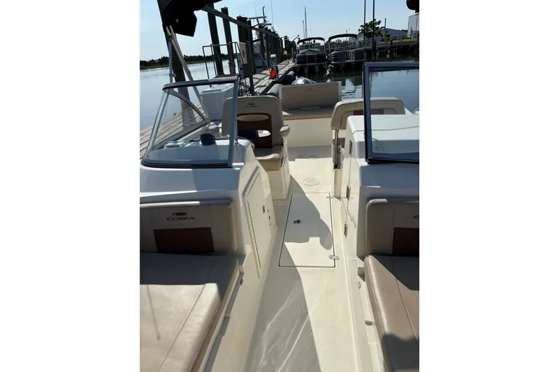 Slide: The Image of 2024 Cobia 220 Dual Console boat interior with seating and windshield, docked by the water. - 4