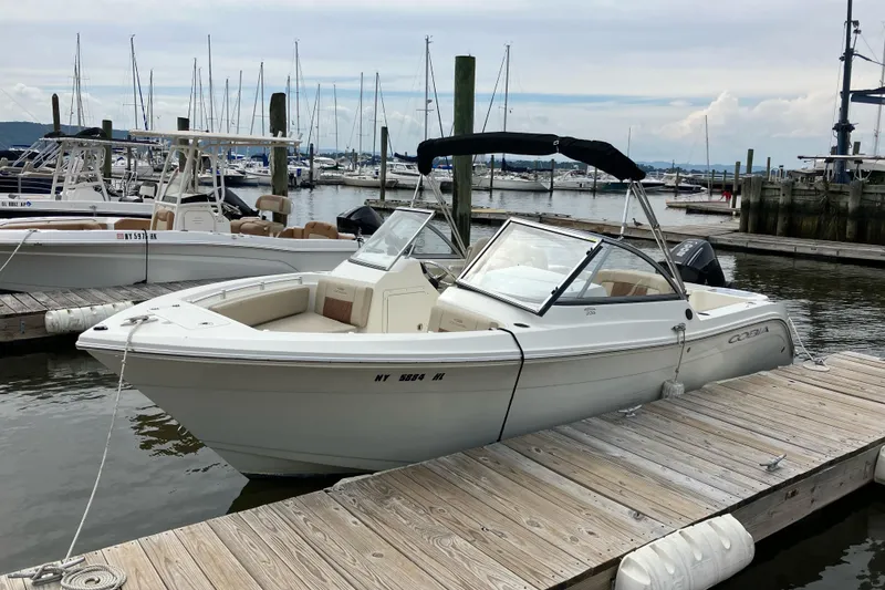 Slide: The Image of 2024 Cobia 220 Dual Console boat docked at marina with sailboats in background. - 2