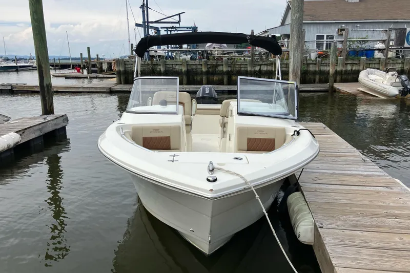 Slide: The Image of 2024 Cobia 220 Dual Console boat docked at a marina, featuring sleek design and spacious seating. - 3