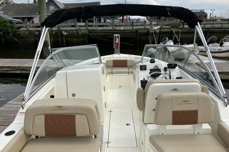 Slide: The Image of 2024 Cobia 220 Dual Console boat interior with beige seating and dashboard, docked at marina. - 6