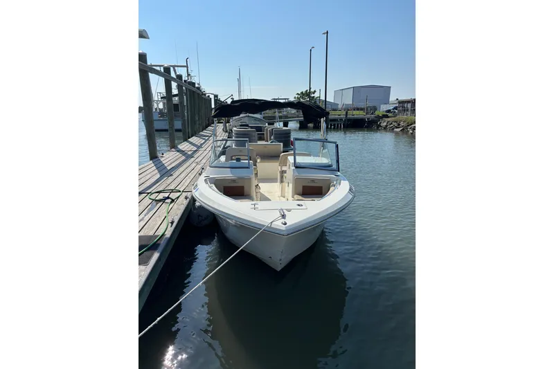 Slide: The Image of 2024 Cobia 220 Dual Console boat docked in a marina under clear skies. - 2