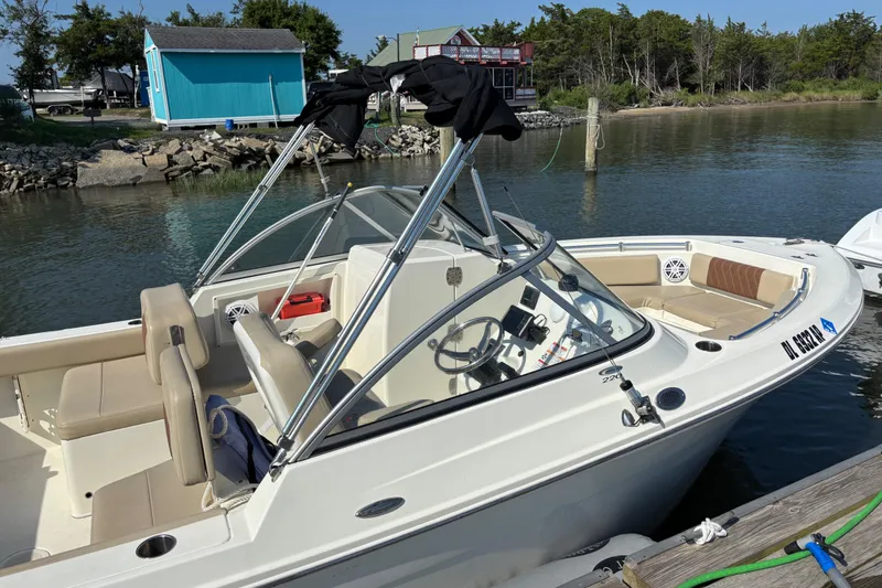 Slide: The Image of 2024 Cobia 220 Dual Console boat docked by a serene waterfront. - 3