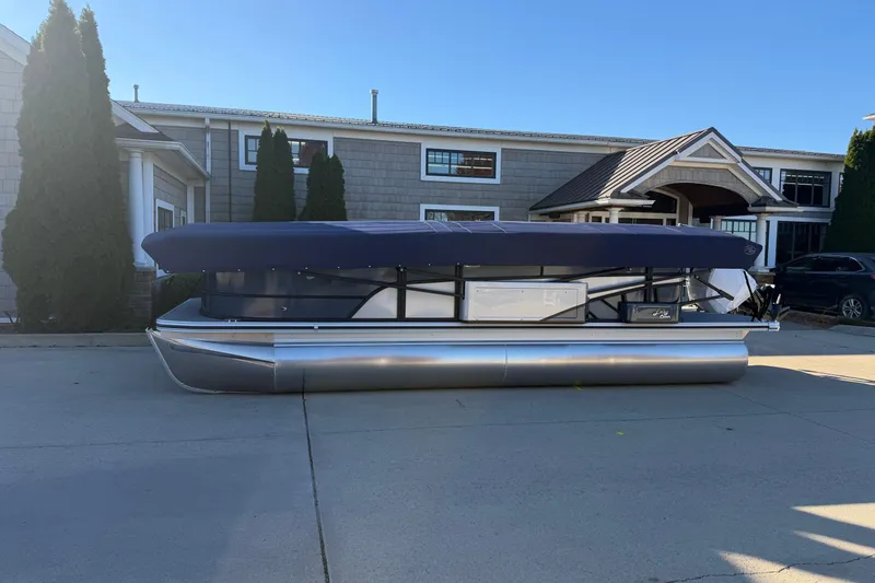 Slide: The Image of 2026 Crest Conquest 230 L pontoon boat with canopy, parked outside a modern building. - 2