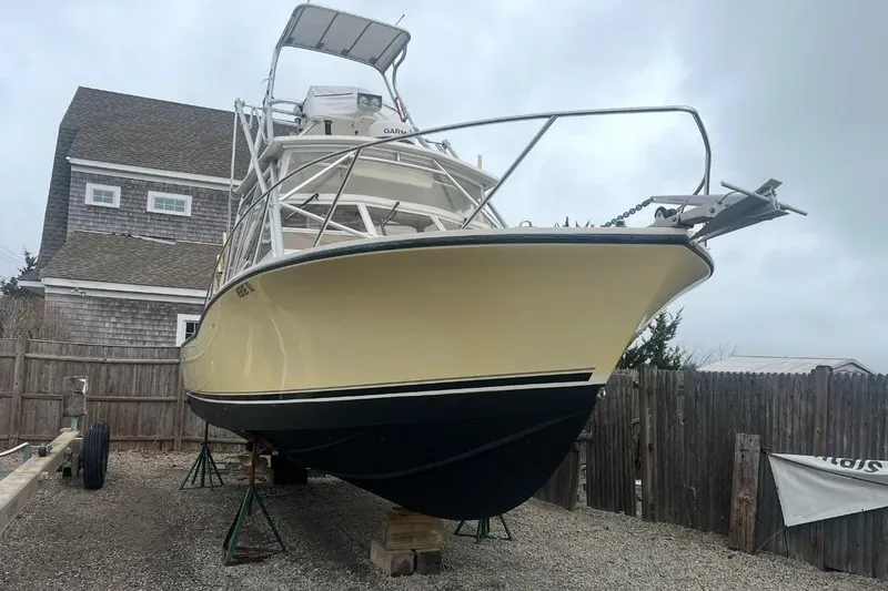 The Image of 2005 Carolina Classic 28 boat on stands, yellow hull, parked near wooden fence. - 0