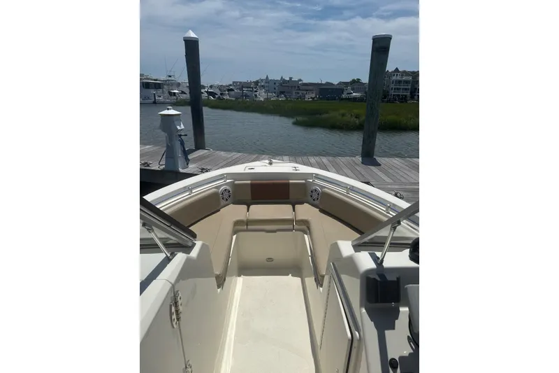 Slide: The Image of 2024 Cobia 220 Dual Console boat docked by a scenic waterfront. - 6