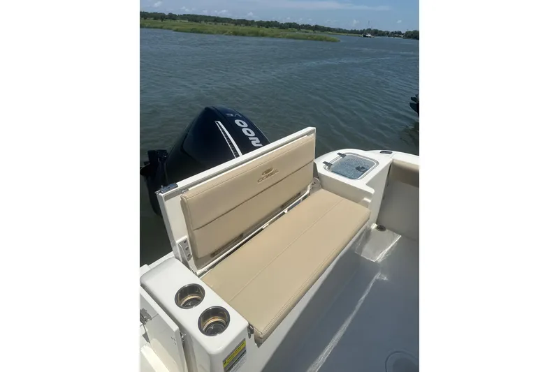 Slide: The Image of 2024 Cobia 220 Dual Console boat with beige seating and cup holders on a calm waterway. - 8
