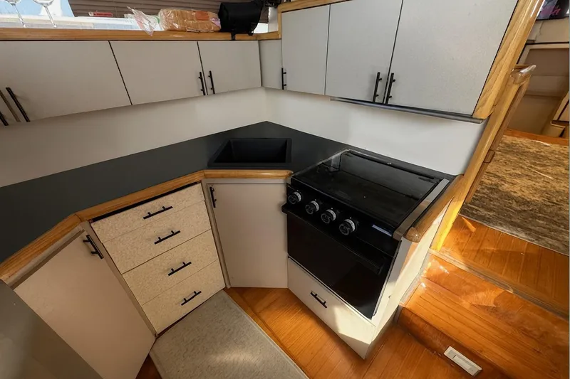 Slide: The Image of 1985 Symbol 58 Cockpit Motor Yacht kitchen with stove, sink, and wooden cabinetry. - 13