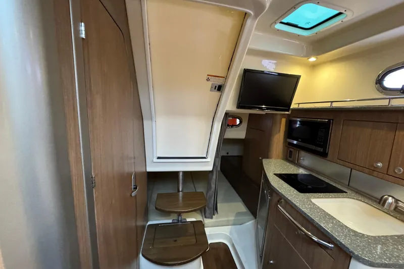 Slide: The Image of 2016 Boston Whaler 315 Conquest cabin interior with kitchenette, TV, and wooden cabinetry. - 27