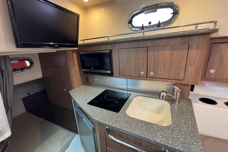 Slide: The Image of 2016 Boston Whaler 315 Conquest interior kitchen with TV, microwave, sink, and stove. - 34