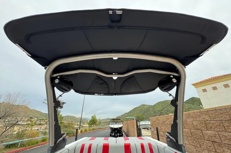 Slide: The Image of 2023 Malibu Wakesetter 21 LX boat with black canopy and speakers, scenic mountain backdrop. - 10