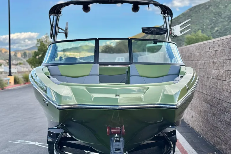 Slide: The Image of 2023 MasterCraft NXT22 boat in green, parked on a road with scenic background. - 2