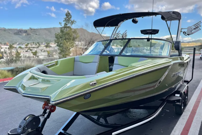 Slide: The Image of 2023 MasterCraft NXT22 boat in green, parked on a trailer with scenic background. - 3