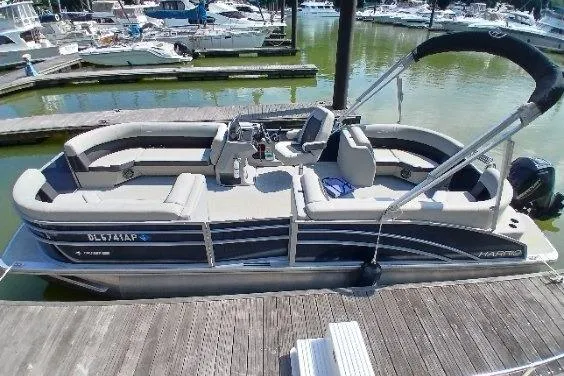 Slide: The Image of 2024 Harris HCX23 pontoon boat docked at marina, featuring spacious seating and modern design. - 2