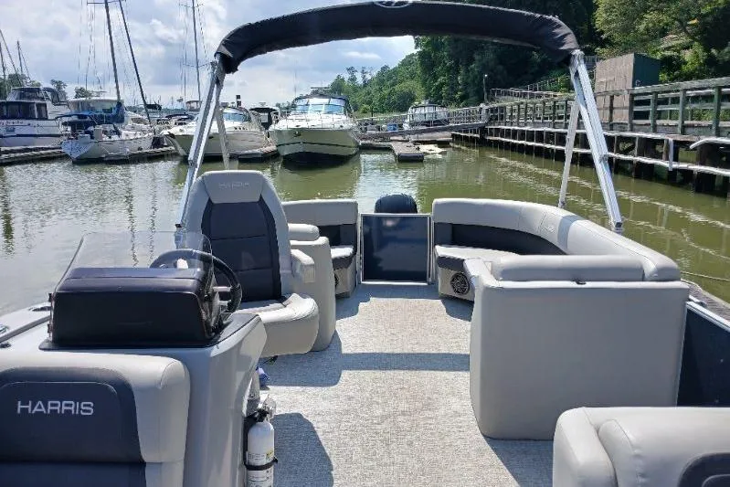 Slide: The Image of 2024 Harris HCX23 pontoon boat docked at a marina, featuring spacious seating and modern design. - 7
