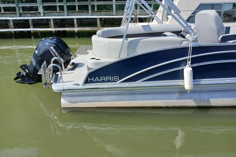 Slide: The Image of 2024 Harris HCX23 pontoon boat with Mercury outboard motor, docked on calm water. - 9