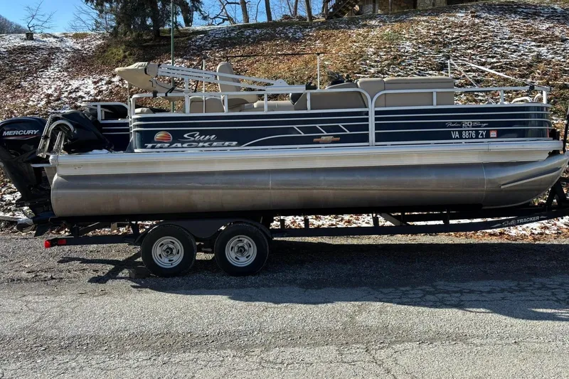 The Image of 2023 Sun Tracker Fishin' Barge 20 DLX pontoon boat on trailer, parked outdoors. - 0