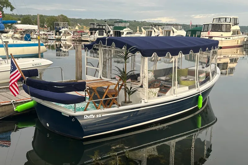 The Image of 2021 Duffy Sun Cruiser 22 docked at marina, featuring blue canopy and American flag. - 0