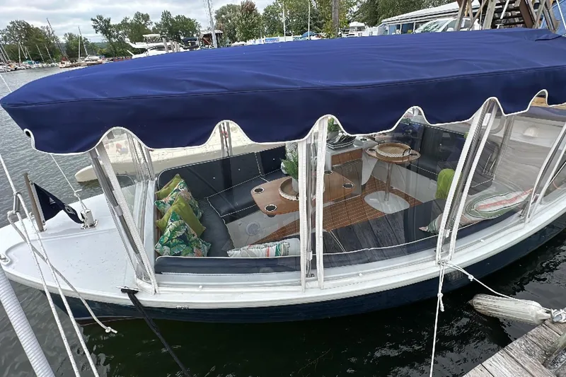 Slide: The Image of 2021 Duffy Sun Cruiser 22 with blue canopy, docked, featuring cozy interior seating. - 3