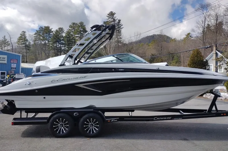 Slide: The Image of 2026 Crownline Eclipse E255 boat on trailer, parked outdoors with trees in background. - 24