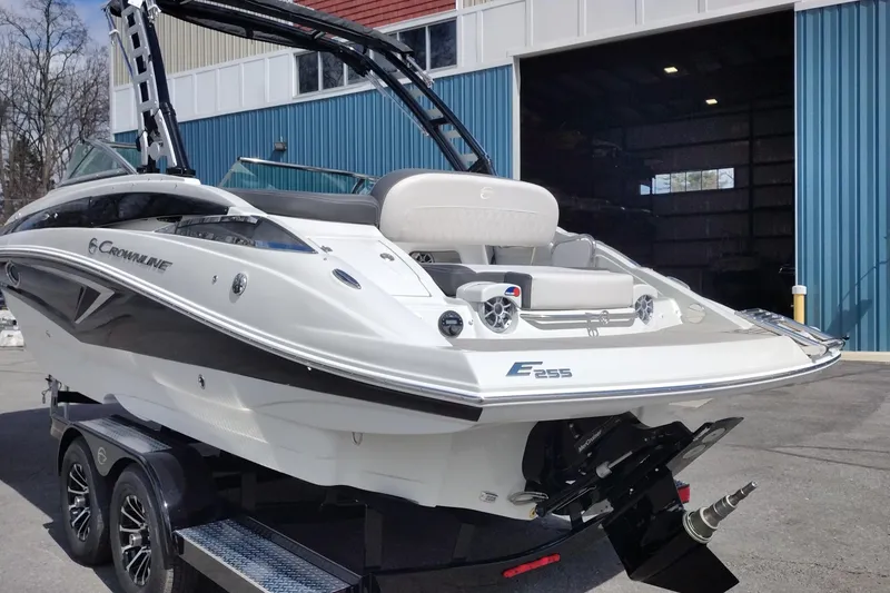 Slide: The Image of 2026 Crownline Eclipse E255 boat on trailer outside a blue warehouse. - 27