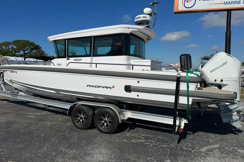 Slide: The Image of 2022 Axopar 28 CABIN boat on trailer, featuring Mercury engine, parked outdoors. - 2