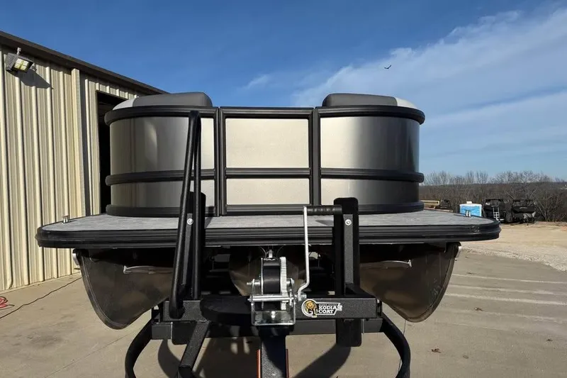 Slide: The Image of 2026 Alera M 25Q pontoon boat on trailer, parked outside a warehouse. - 2