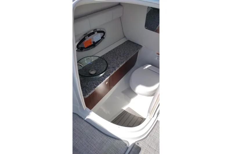 Slide: The Image of Interior of 2026 Crownline 260 XSS boat featuring a compact bathroom with granite countertop. - 17