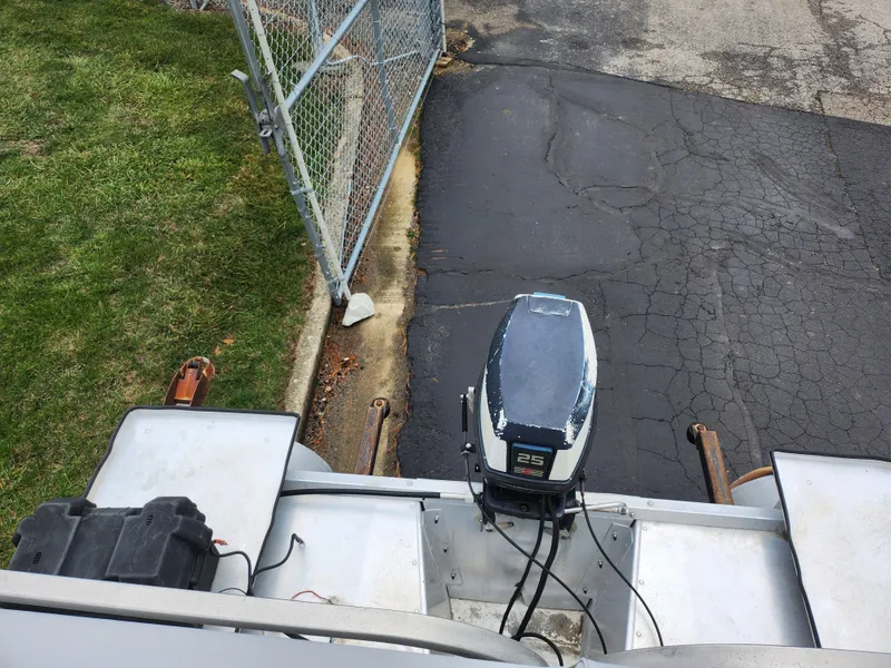 Slide: The Image of 1991 Grumman Fish N Fun boat with outboard motor, parked near a fence. - 14