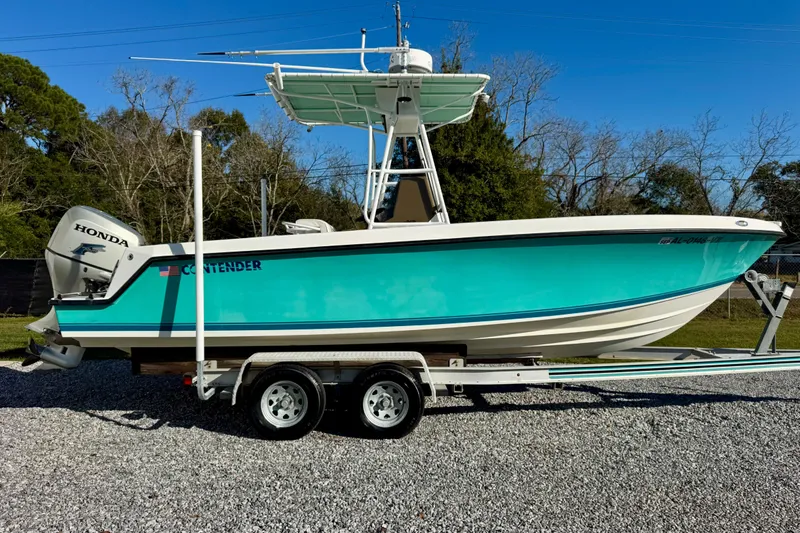 Slide: The Image of 2000 Contender 23 Open boat on trailer with Honda outboard, turquoise hull, clear sky background. - 2