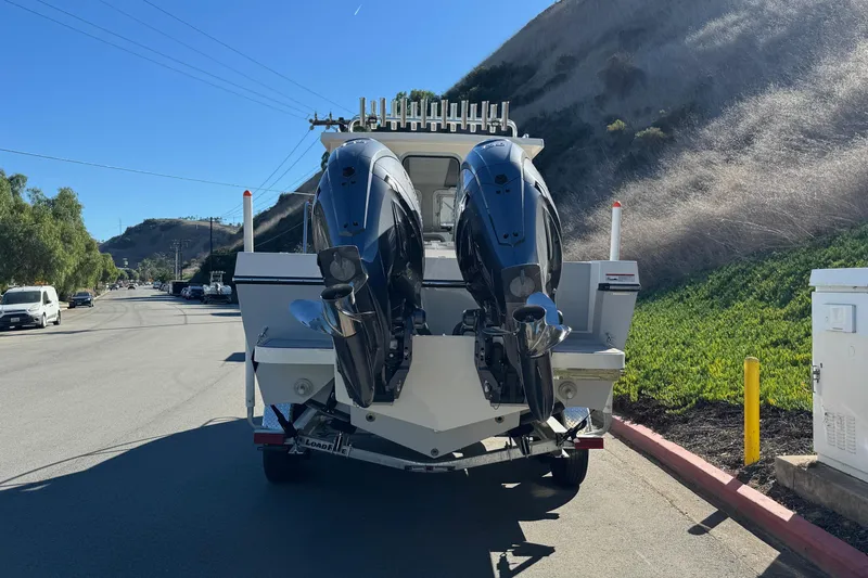 Slide: The Image of 2026 Defiance Admiral 250 EX boat with dual engines on a trailer, parked on a sunny street. - 12