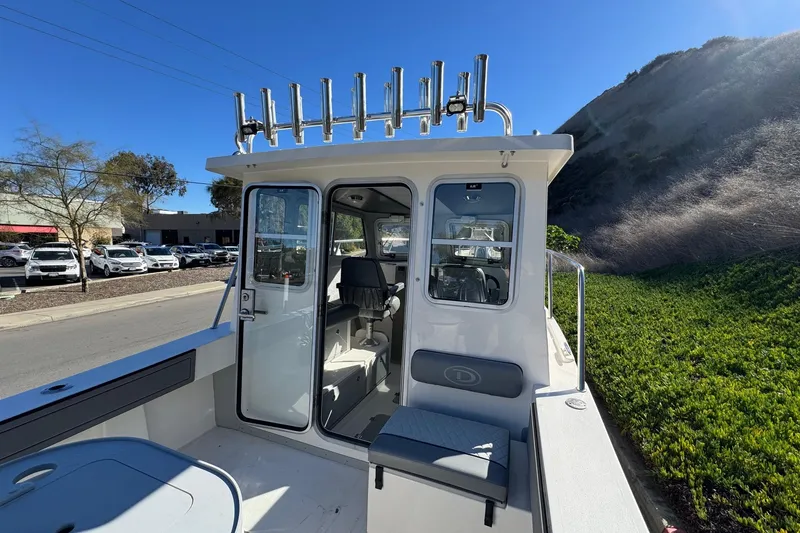 Slide: The Image of 2026 Defiance Admiral 250 EX boat with open cabin and rod holders, parked outdoors. - 49