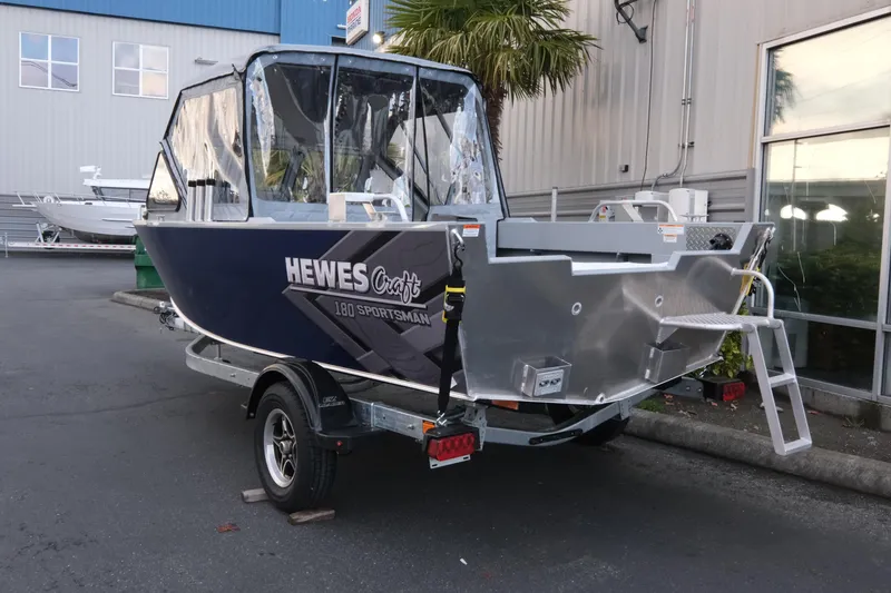 Slide: The Image of 2026 Hewescraft 180 Sportsman boat on trailer, parked outside a building. - 4